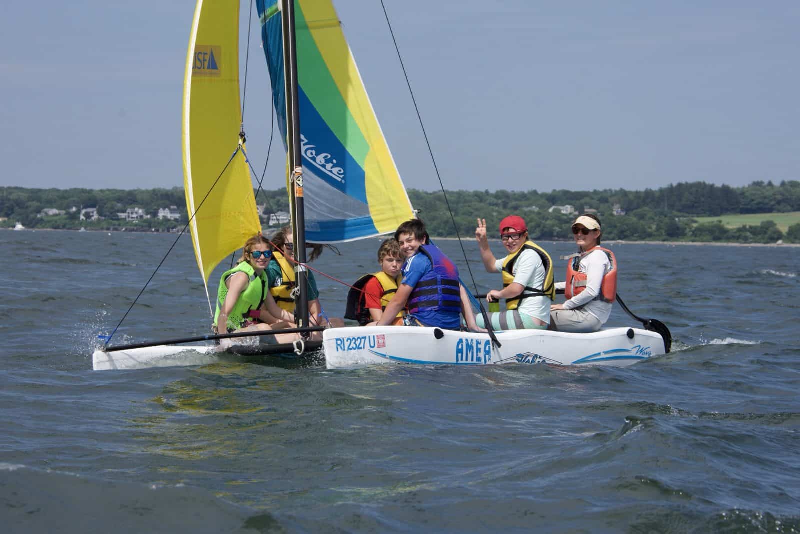 An instructor and four campers sailing a Hobie under a blue-and-yellow sail