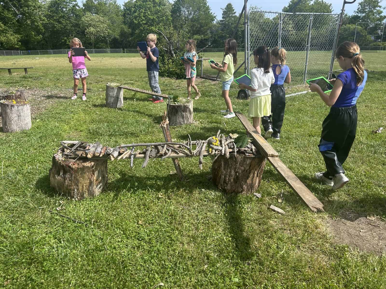 A Jamestown class building a stick-and-plank structure across stumps on the school field