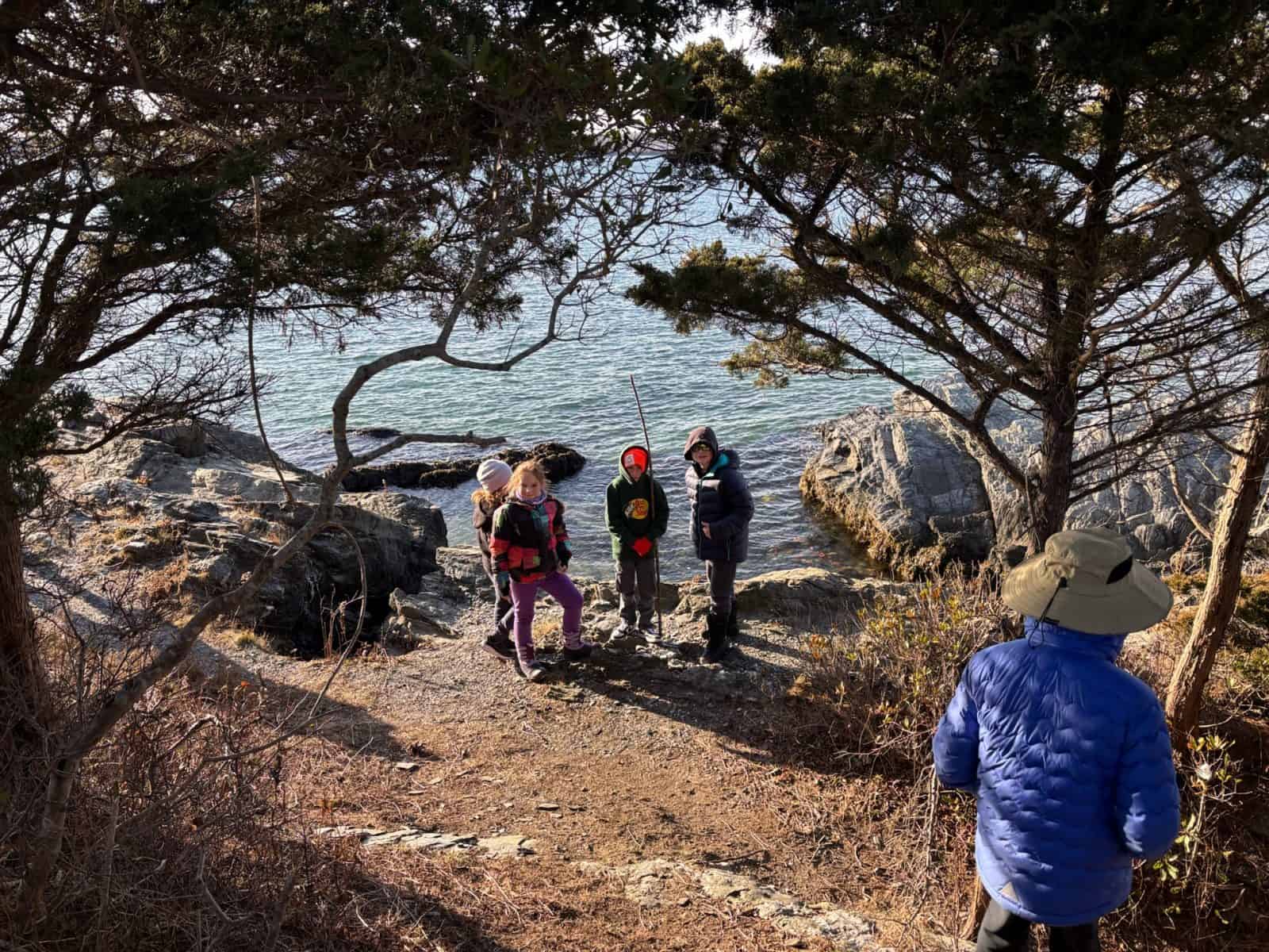 Kids exploring a juniper-framed cove at Fort Getty while a guide watches