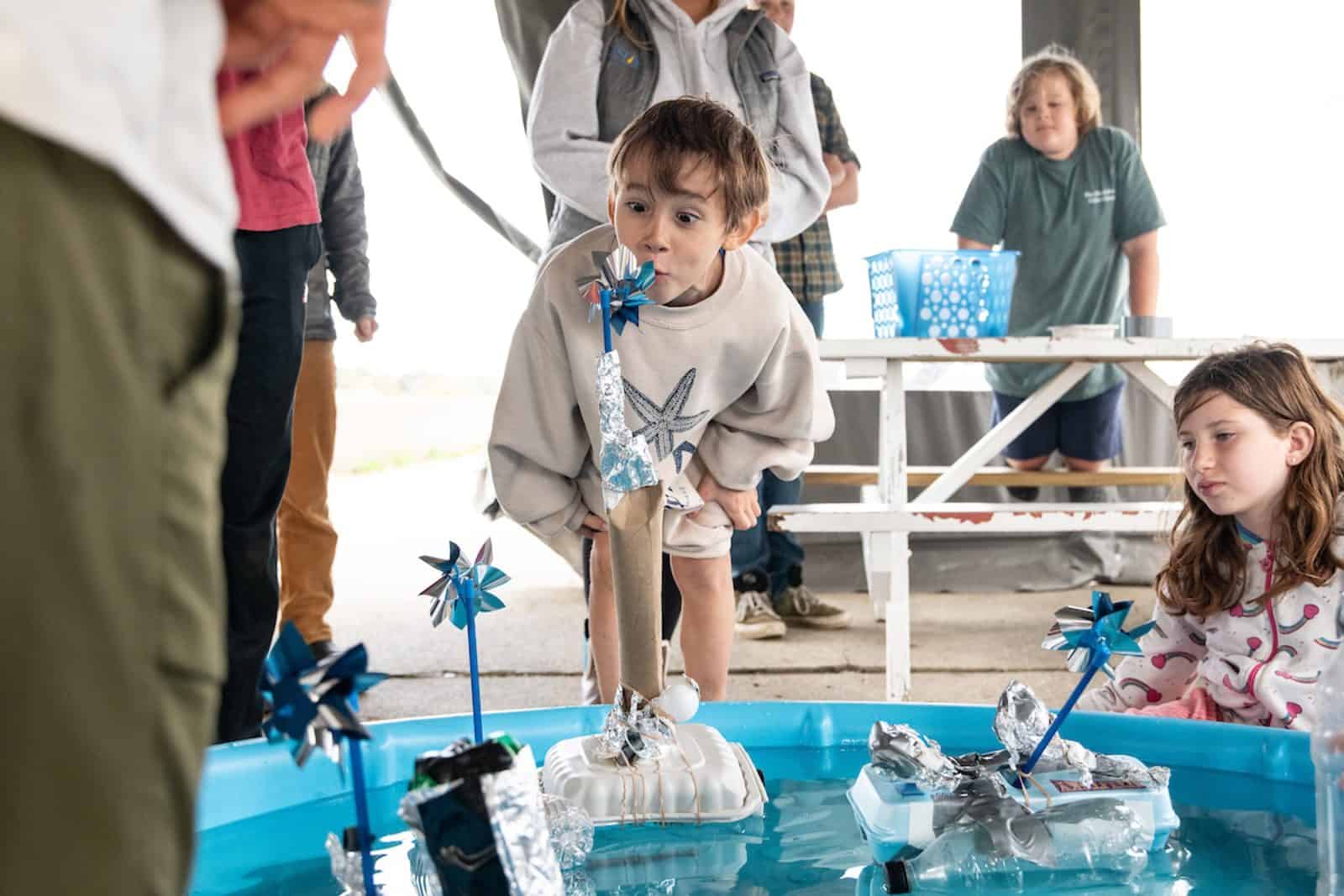 A homeschool student testing a floating wind-turbine model built from recycled materials, in a CISF program with US Sailing