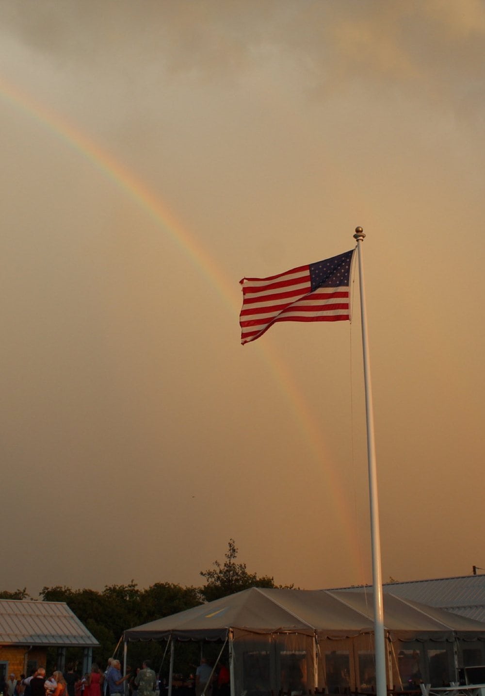 A double rainbow over the American flag and the event tents at CISF's 2026 Summer Party, after the storm